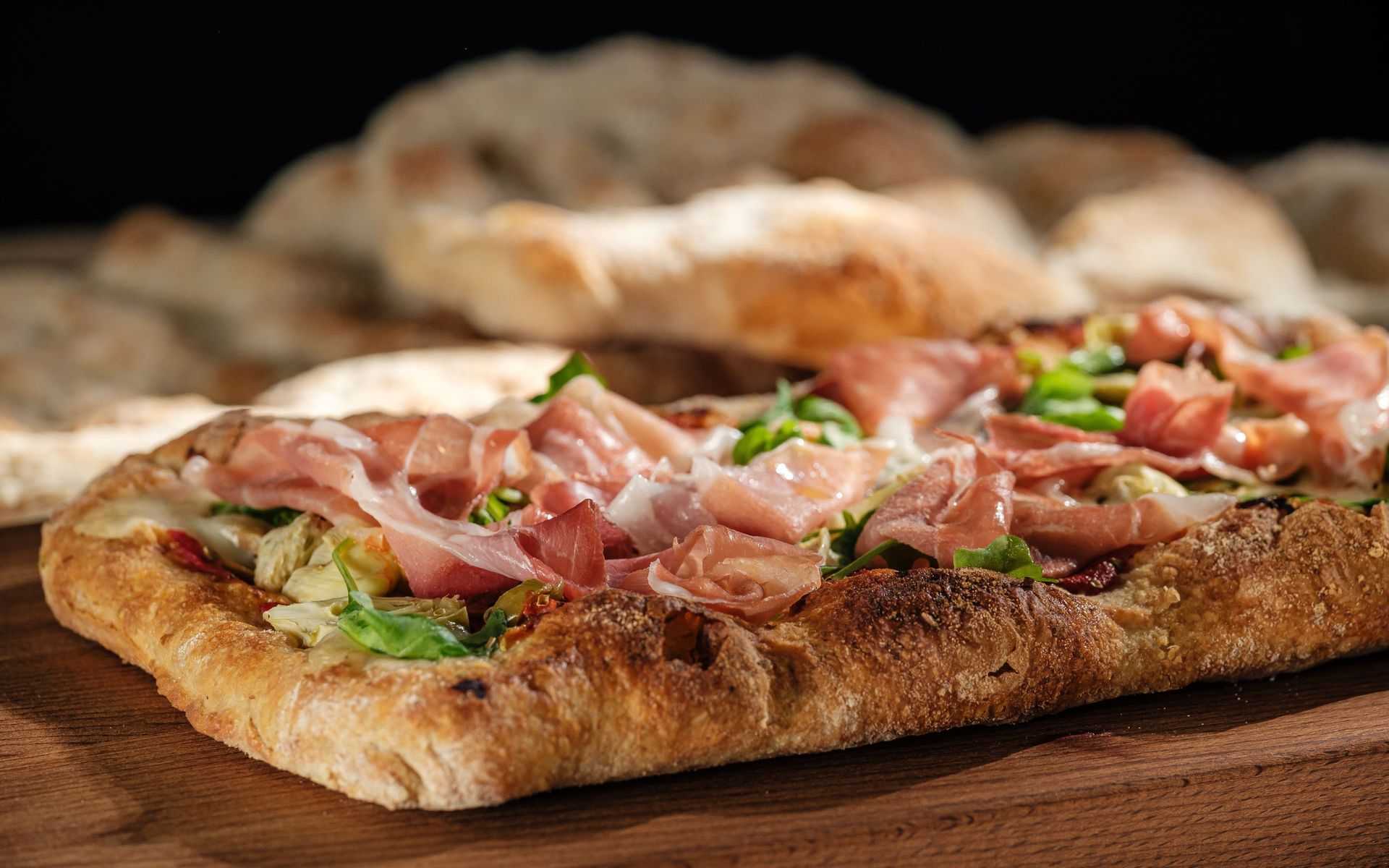 Rustic wholegrain flatbread with prosciutto, artichokes and arugula on wooden board