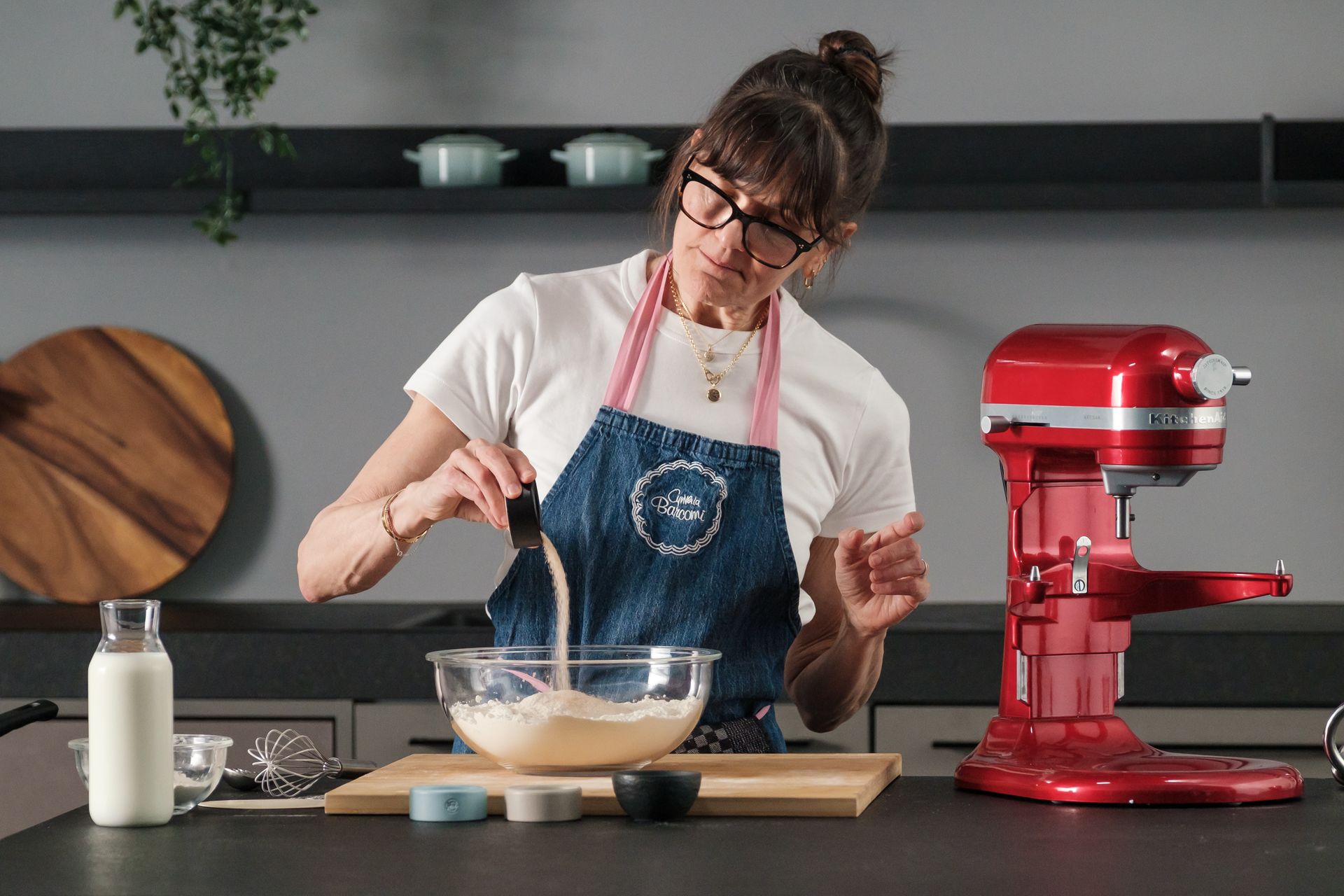 Baker in apron pouring sugar into glass mixing bowl next to red stand mixer — baking course, vegetarian