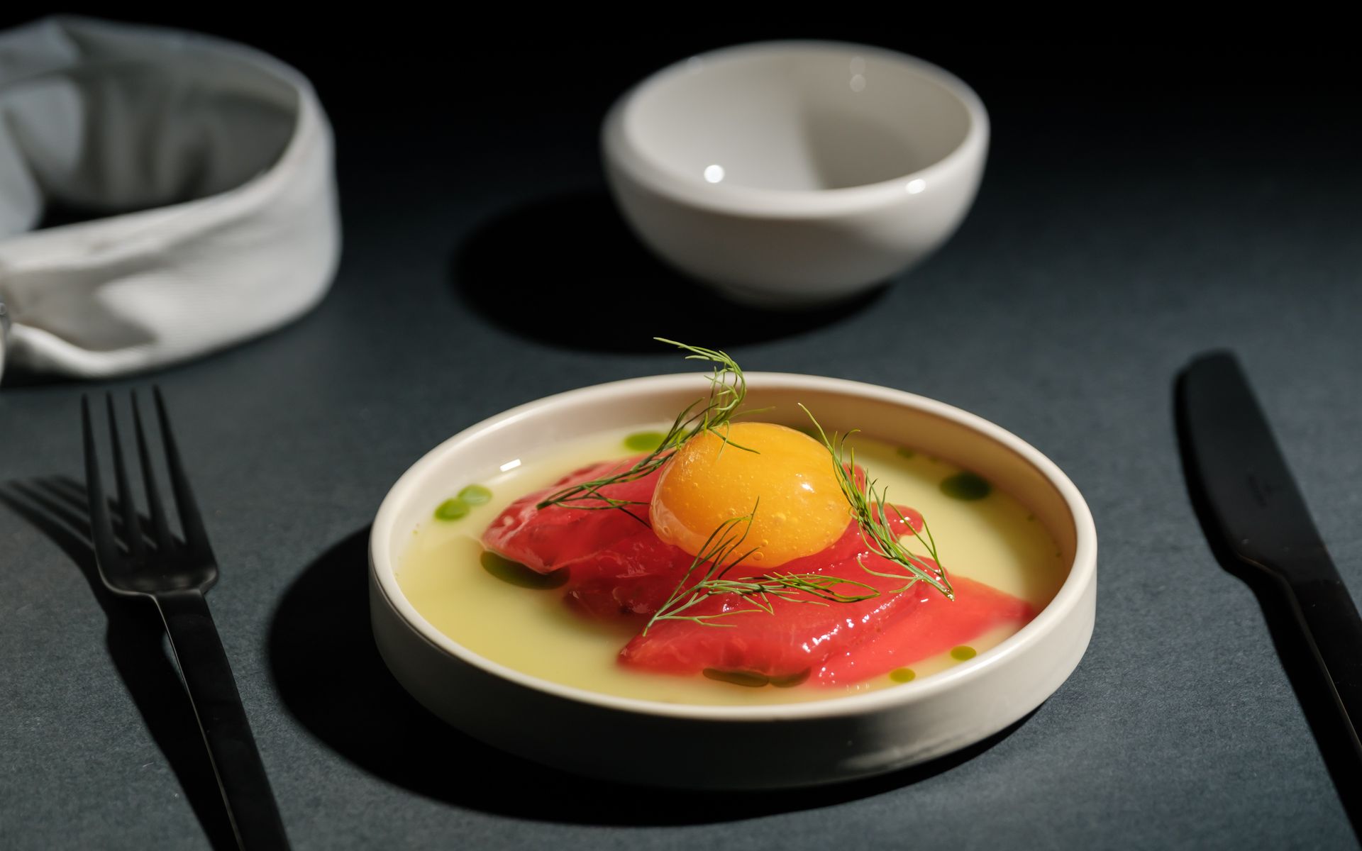 Watermelon 'tuna' with mango yolk, parmesan emulsion and dill in a white bowl