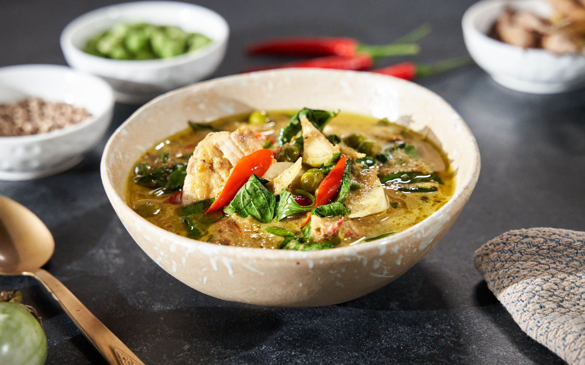 Thai green curry with chicken, vegetables, and red chili peppers in a bowl.