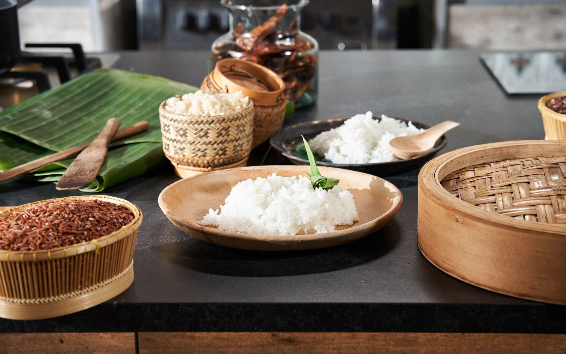 Various rice types in baskets and bamboo steamer on kitchen countertop