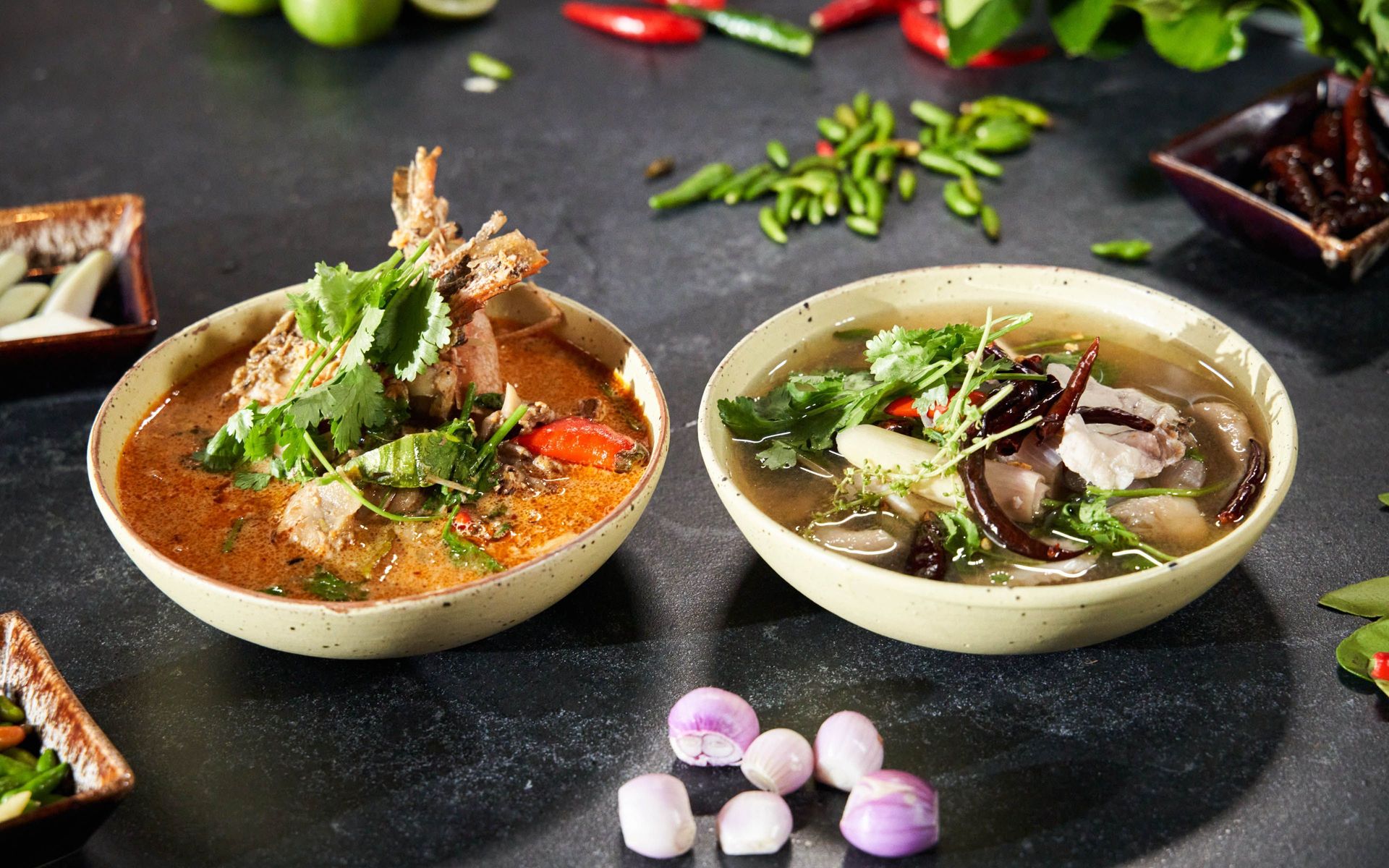 Thai soups with chili and herbs on a black table.